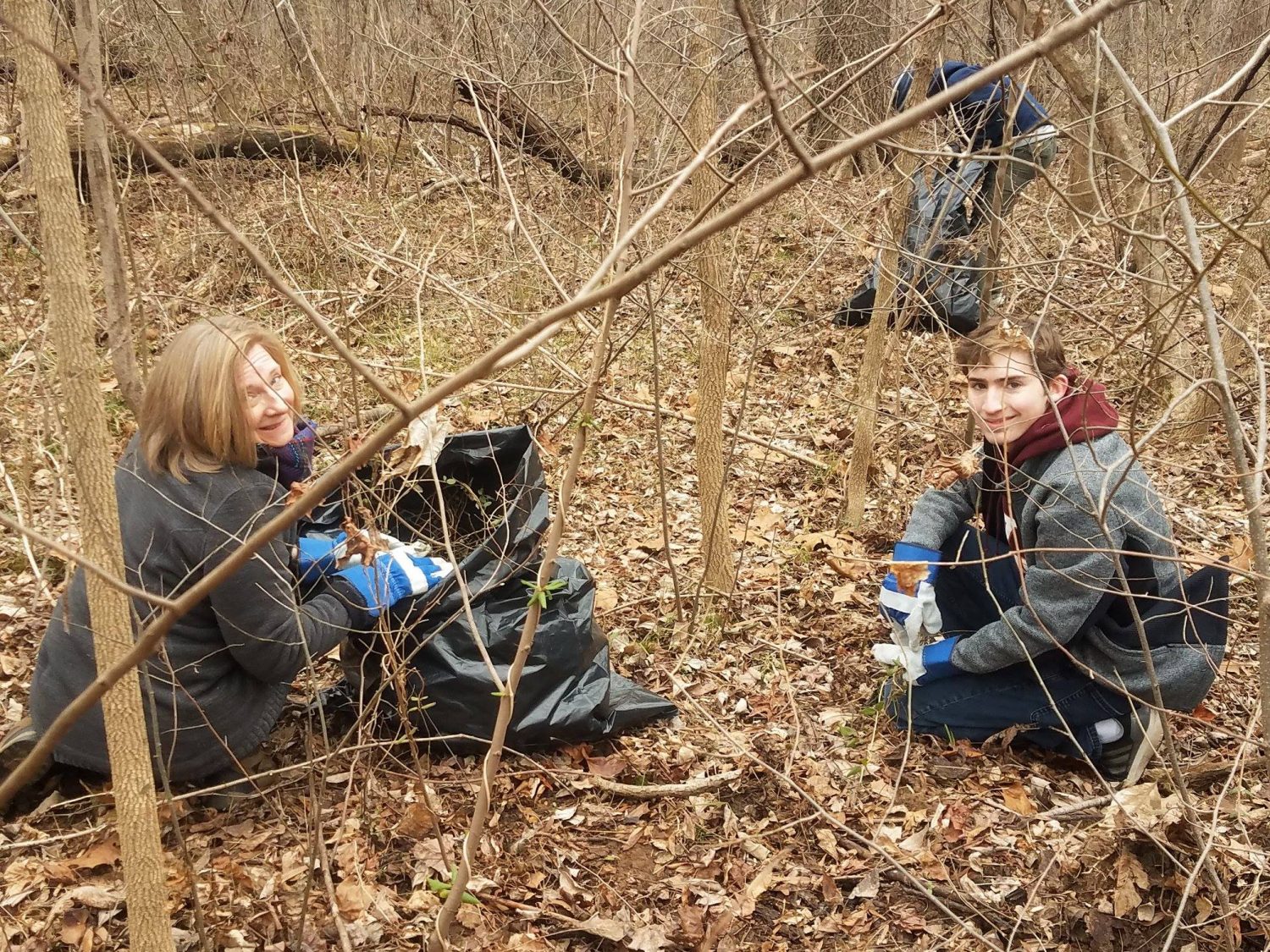 volunteers kneeling in woods with trashbags